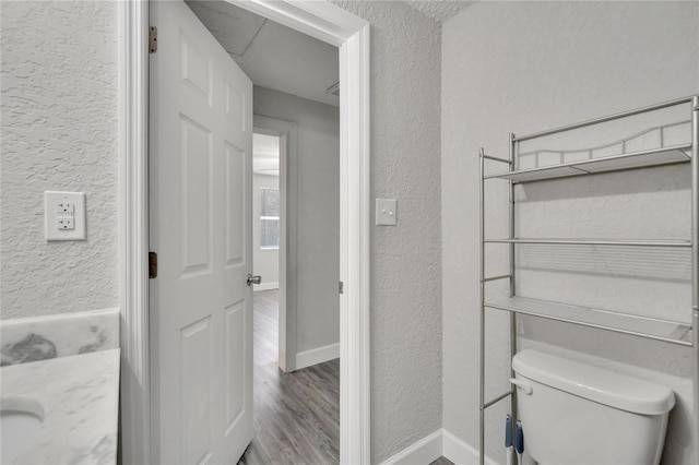 bathroom featuring a textured wall, baseboards, wood finished floors, and toilet