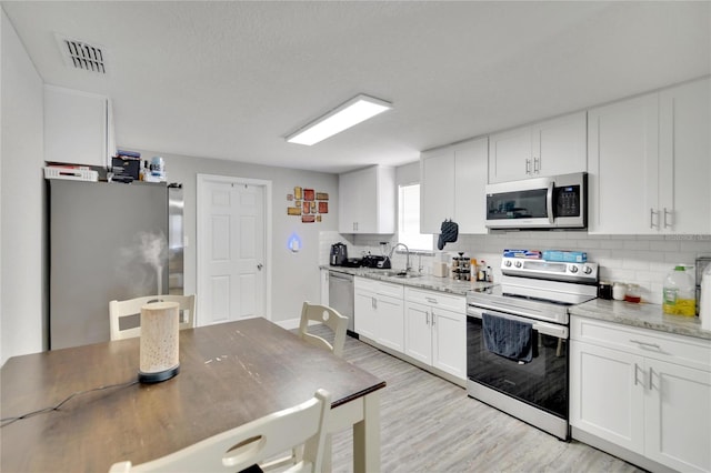 kitchen with decorative backsplash, appliances with stainless steel finishes, light stone countertops, white cabinetry, and light hardwood / wood-style flooring