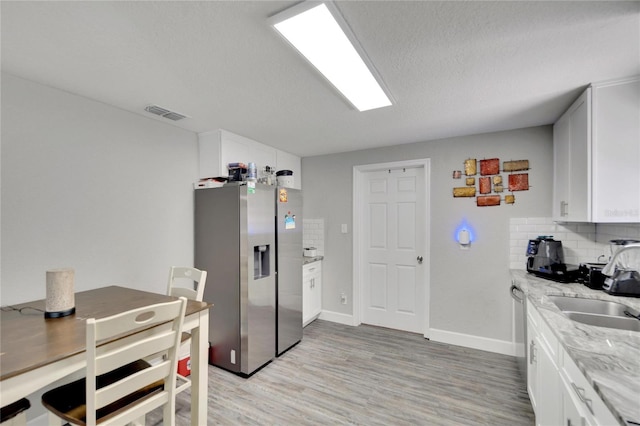 kitchen with tasteful backsplash, a sink, light wood-style floors, stainless steel refrigerator with ice dispenser, and light stone countertops