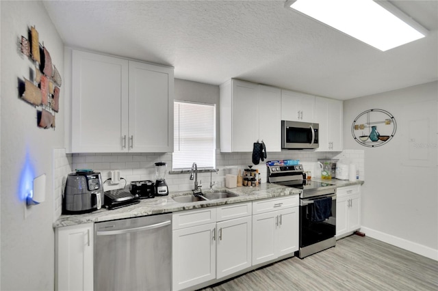 kitchen featuring white cabinetry, appliances with stainless steel finishes, backsplash, light wood-type flooring, and sink