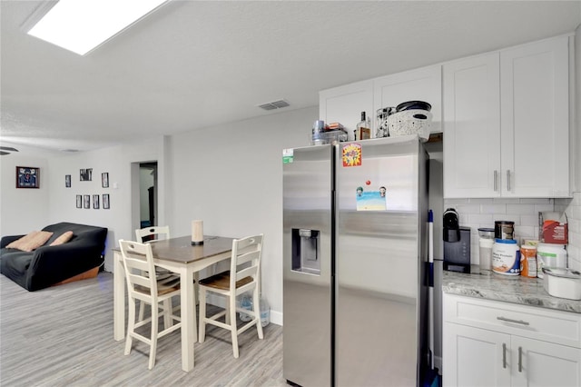 kitchen with decorative backsplash, light hardwood / wood-style flooring, light stone counters, white cabinetry, and stainless steel refrigerator with ice dispenser