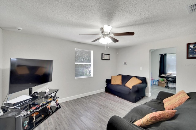 living room with ceiling fan, light wood-type flooring, and a textured ceiling