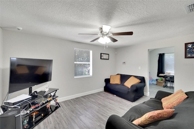 living room featuring wood finished floors, visible vents, a ceiling fan, baseboards, and a textured ceiling