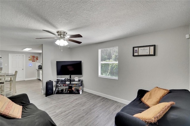 living room featuring wood finished floors, a textured ceiling, baseboards, and ceiling fan