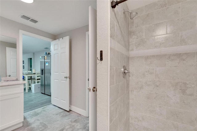 bathroom featuring a tile shower, vanity, and wood-type flooring