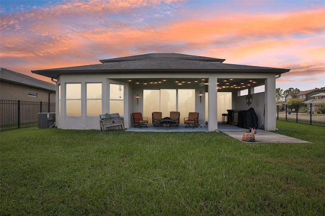 back house at dusk with a patio area, central air condition unit, and a yard