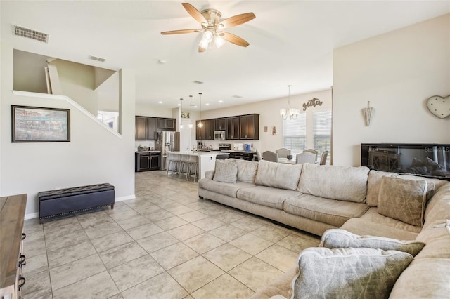 living area featuring light tile patterned floors, visible vents, baseboards, and ceiling fan with notable chandelier