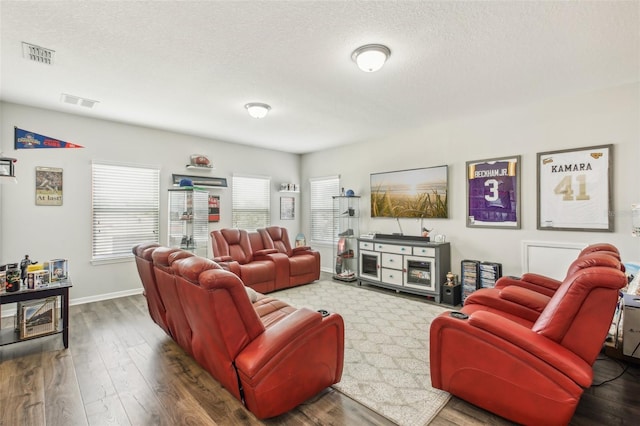 living area featuring visible vents, baseboards, a textured ceiling, and wood finished floors