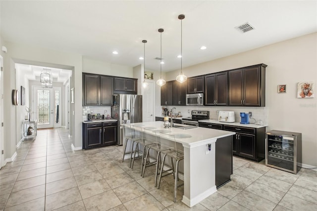 kitchen featuring appliances with stainless steel finishes, wine cooler, a breakfast bar, decorative light fixtures, and a center island with sink