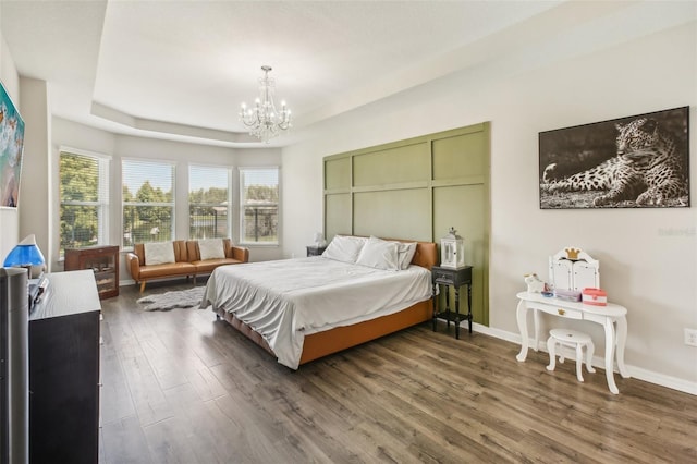 bedroom featuring a notable chandelier, baseboards, a tray ceiling, and wood finished floors