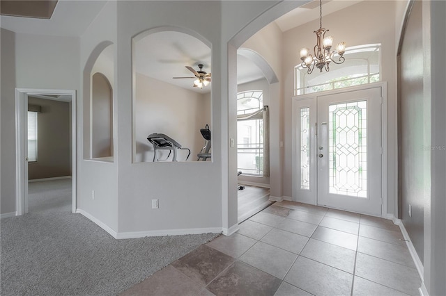 foyer entrance featuring tile patterned floors, arched walkways, ceiling fan with notable chandelier, and baseboards