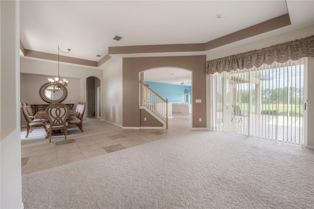 unfurnished living room with a tray ceiling, stairway, carpet, tile patterned floors, and arched walkways