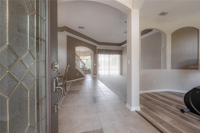 foyer entrance with stairway, light tile patterned floors, baseboards, arched walkways, and visible vents