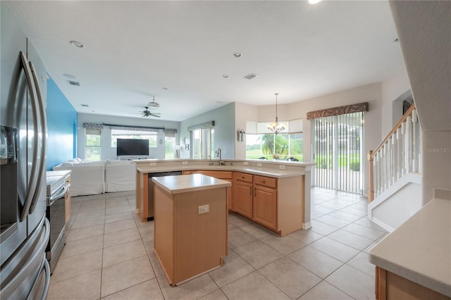 kitchen with light countertops, a kitchen island, appliances with stainless steel finishes, ceiling fan with notable chandelier, and light brown cabinetry