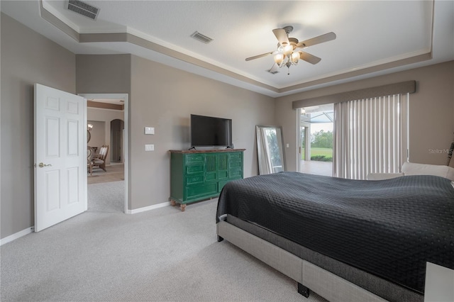 carpeted bedroom with a raised ceiling, arched walkways, baseboards, and visible vents