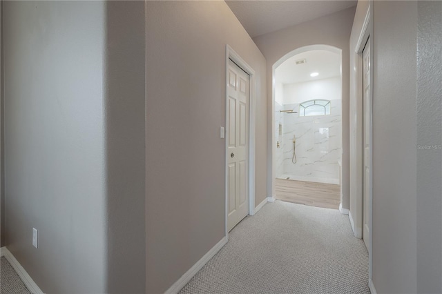 corridor with baseboards, arched walkways, and carpet flooring