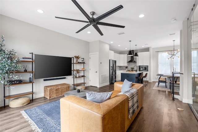 living area with ceiling fan with notable chandelier, visible vents, recessed lighting, and wood finished floors