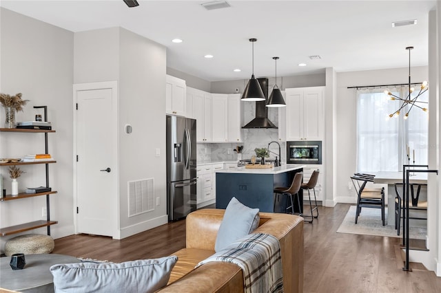 kitchen featuring visible vents, stainless steel fridge with ice dispenser, light countertops, built in microwave, and a center island with sink