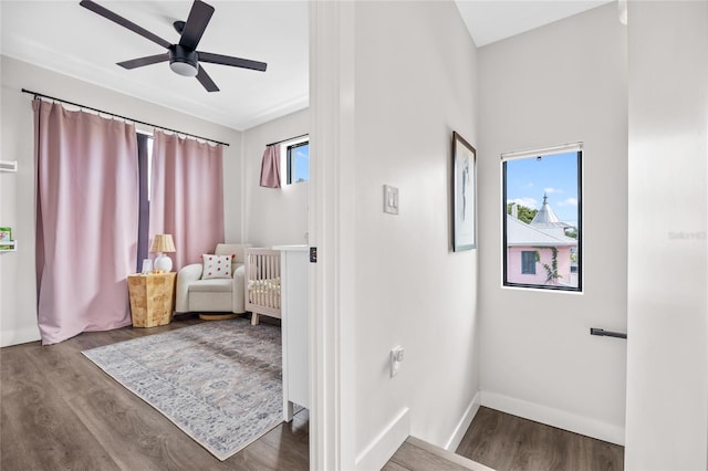 interior space with a nursery area, ceiling fan, wood finished floors, and baseboards