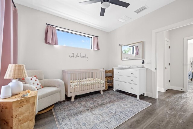 bedroom with a nursery area, dark wood finished floors, visible vents, and baseboards