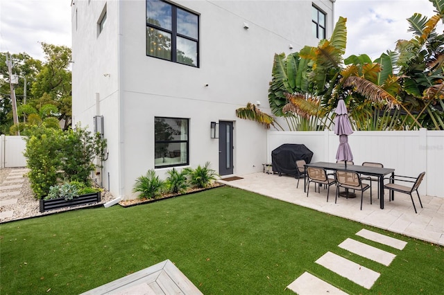 rear view of property with a yard, stucco siding, fence, and a patio