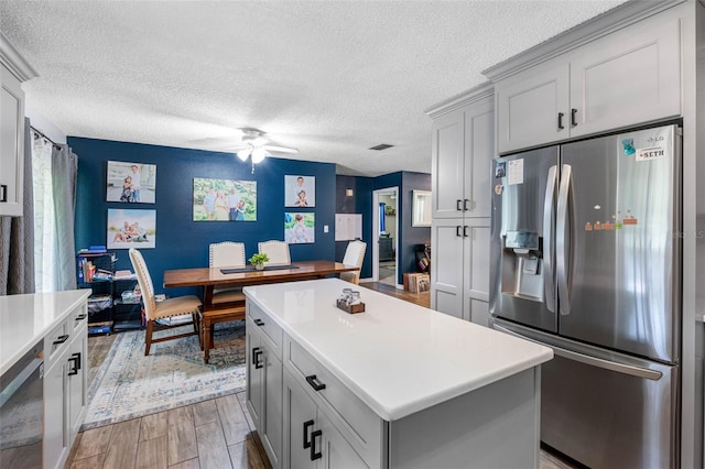 kitchen featuring stainless steel refrigerator with ice dispenser, light wood-type flooring, gray cabinetry, a center island, and ceiling fan