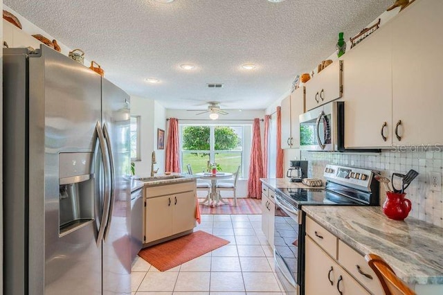 kitchen with a textured ceiling, backsplash, appliances with stainless steel finishes, sink, and ceiling fan