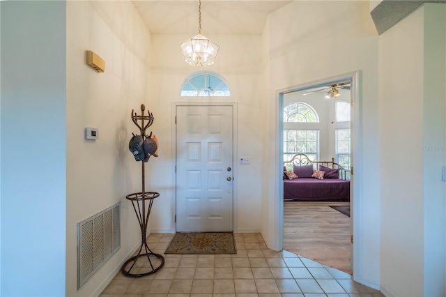 entryway featuring light colored carpet, a high ceiling, and ceiling fan with notable chandelier