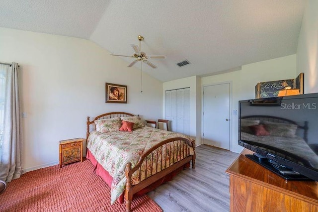 bedroom with hardwood / wood-style flooring, lofted ceiling, a closet, ceiling fan, and a textured ceiling