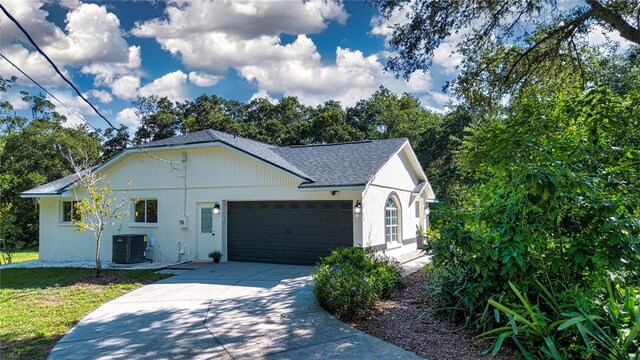 single story home with cooling unit, a garage, concrete driveway, roof with shingles, and stucco siding