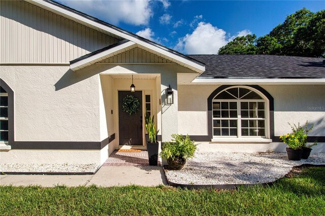 entrance to property featuring a shingled roof and stucco siding