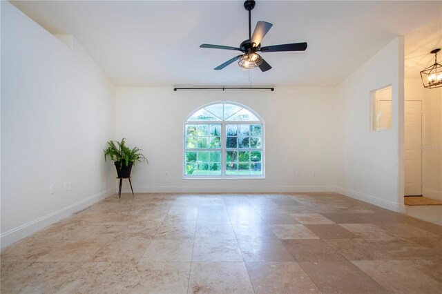 empty room featuring lofted ceiling, baseboards, and ceiling fan with notable chandelier