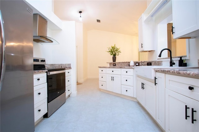 kitchen with light tile patterned flooring, light stone counters, stainless steel appliances, wall chimney range hood, and white cabinets