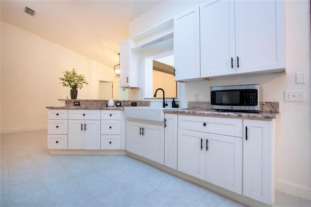 kitchen featuring a peninsula, a sink, visible vents, white cabinetry, and stainless steel microwave