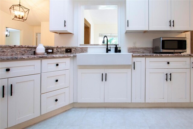 kitchen featuring white cabinetry, stainless steel microwave, pendant lighting, and a sink