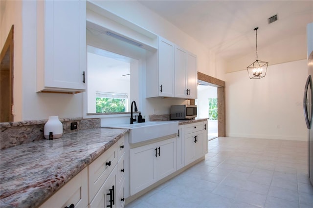 kitchen featuring light stone countertops, stainless steel microwave, white cabinets, and a sink