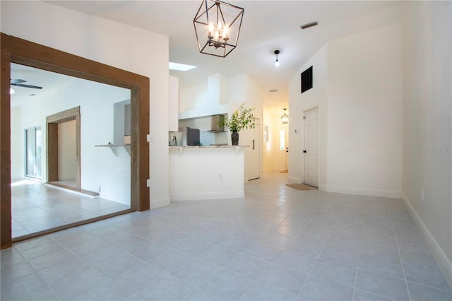 empty room with vaulted ceiling, ceiling fan with notable chandelier, light tile patterned flooring, and baseboards