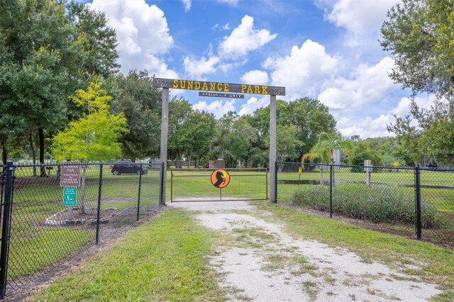 view of property's community featuring dirt driveway, a lawn, fence, and a gate