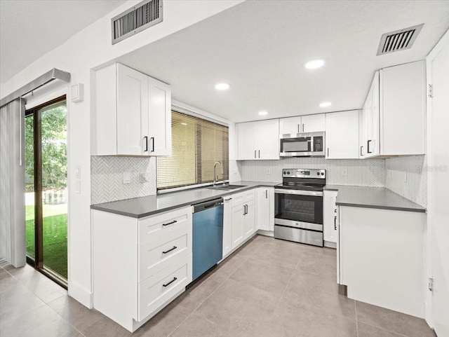 kitchen with appliances with stainless steel finishes, tasteful backsplash, light tile patterned floors, and white cabinets