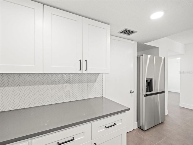 kitchen with stainless steel refrigerator with ice dispenser, white cabinetry, light tile patterned floors, and tasteful backsplash