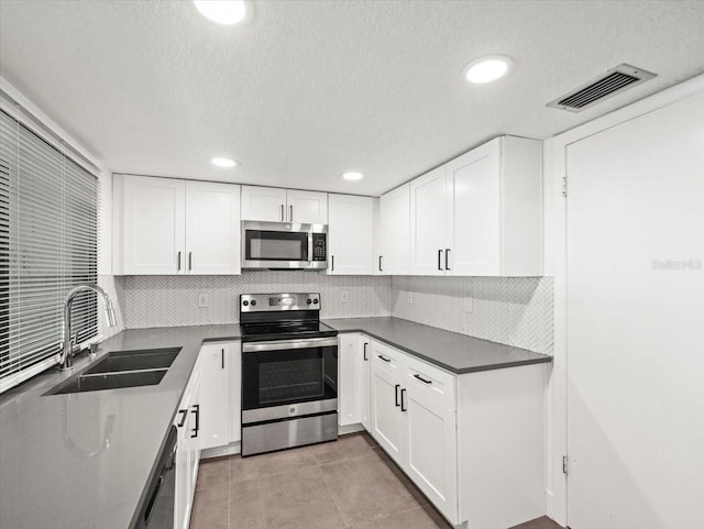 kitchen with stainless steel appliances, sink, white cabinetry, and light tile patterned flooring