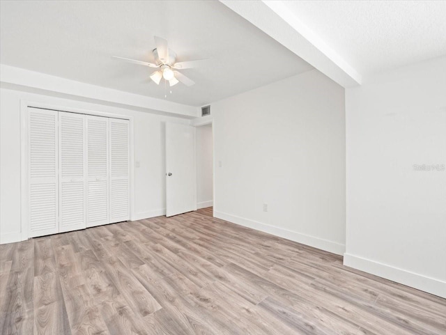 unfurnished bedroom featuring a closet, ceiling fan, light hardwood / wood-style floors, and beam ceiling