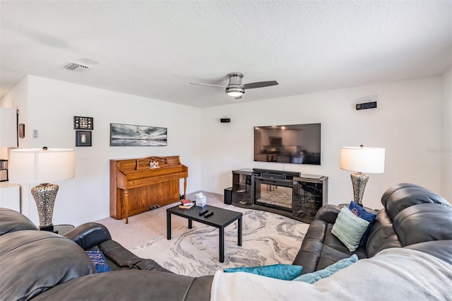 carpeted living room with ceiling fan, a textured ceiling, and a fireplace