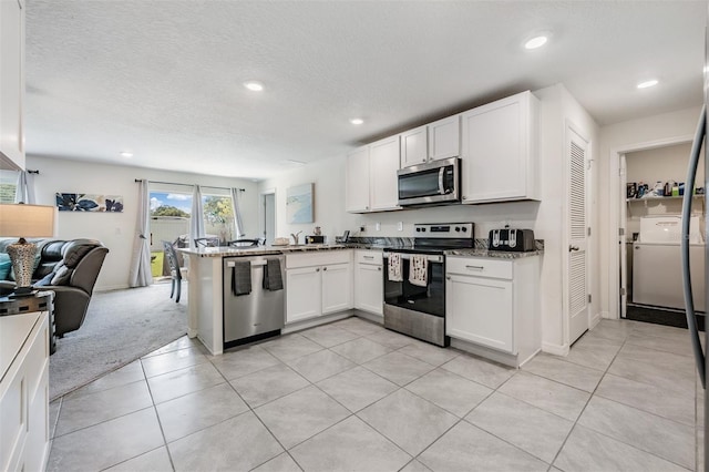 kitchen featuring light carpet, washer / clothes dryer, white cabinets, appliances with stainless steel finishes, and kitchen peninsula