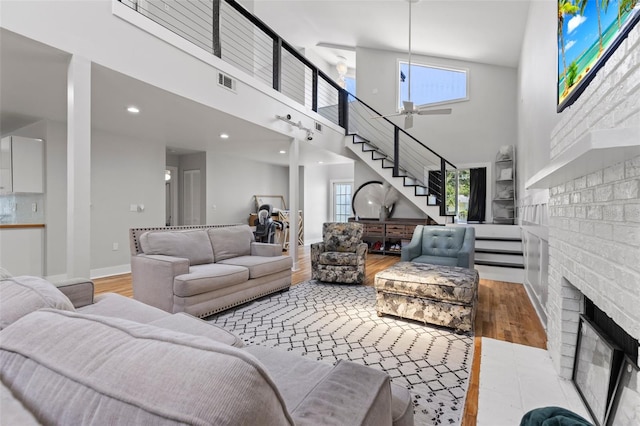 living room with a fireplace, light hardwood / wood-style flooring, a high ceiling, and ceiling fan