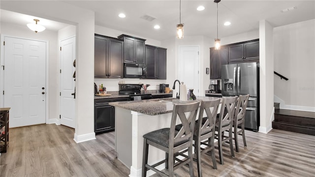 kitchen featuring pendant lighting, black appliances, a kitchen breakfast bar, a center island with sink, and sink