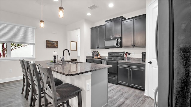 kitchen with a kitchen breakfast bar, dark stone countertops, an island with sink, decorative light fixtures, and black appliances