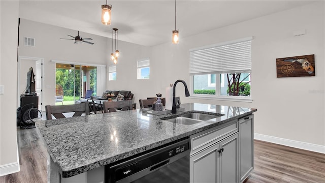 kitchen featuring sink, stainless steel dishwasher, an island with sink, decorative light fixtures, and light stone counters