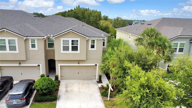 townhome / multi-family property with a garage, concrete driveway, a shingled roof, and stucco siding