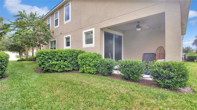 view of home's exterior featuring a lawn, a ceiling fan, and stucco siding